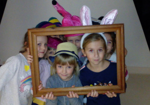 Dziewczynki w kolorowych nakryciach głowy pozują do zdjęcia w ramie obrazu.